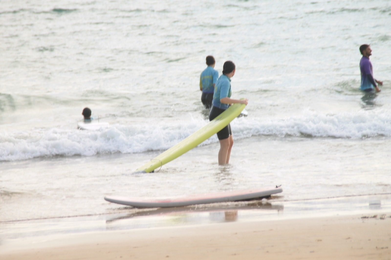 Alumna con tabla de surf en la orilla sonriendo en Zahara de los Atunes